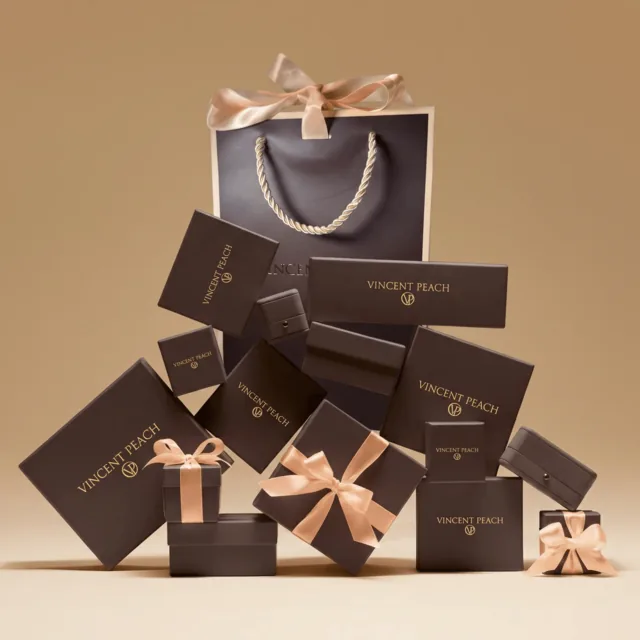 Brown Vincent Peach gift boxes embossed with the gold VP monogram, hand-tied with cream satin ribbons, stacked beside the signature shopping bag.